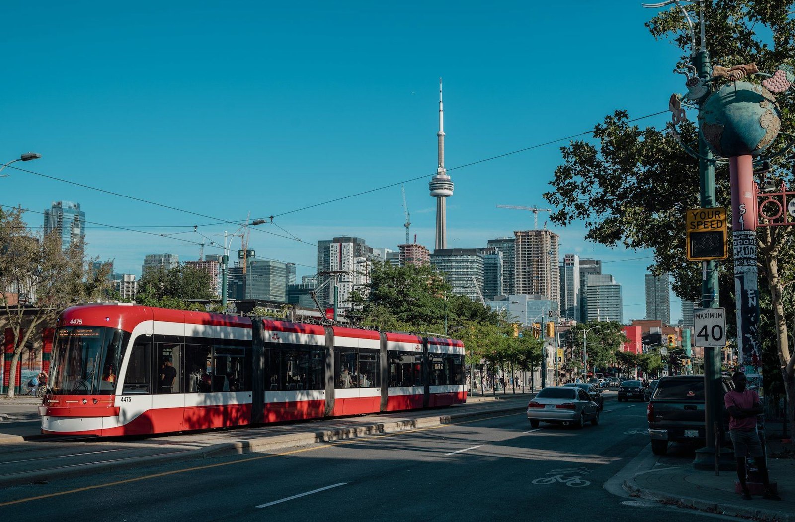 A red and white streetcar on a sunny Toronto street, with the CN Tower and downtown skyline behind it