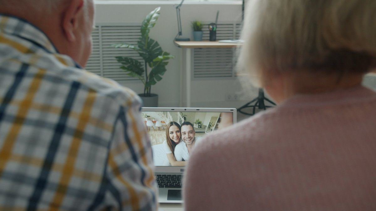 Un couple âgé, vu de dos, en appel vidéo sur un ordinateur portable avec un jeune couple souriant