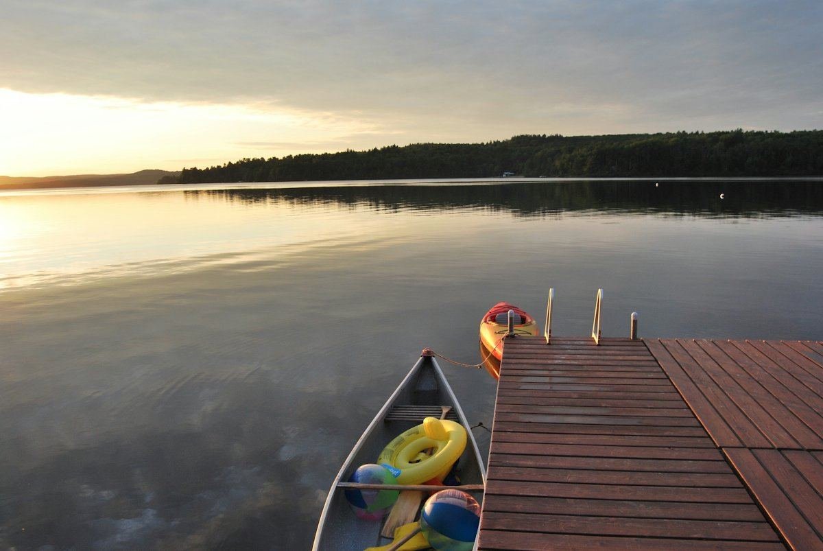 Un canot posé près d’un quai de bois, sur un lac immobile au coucher du soleil