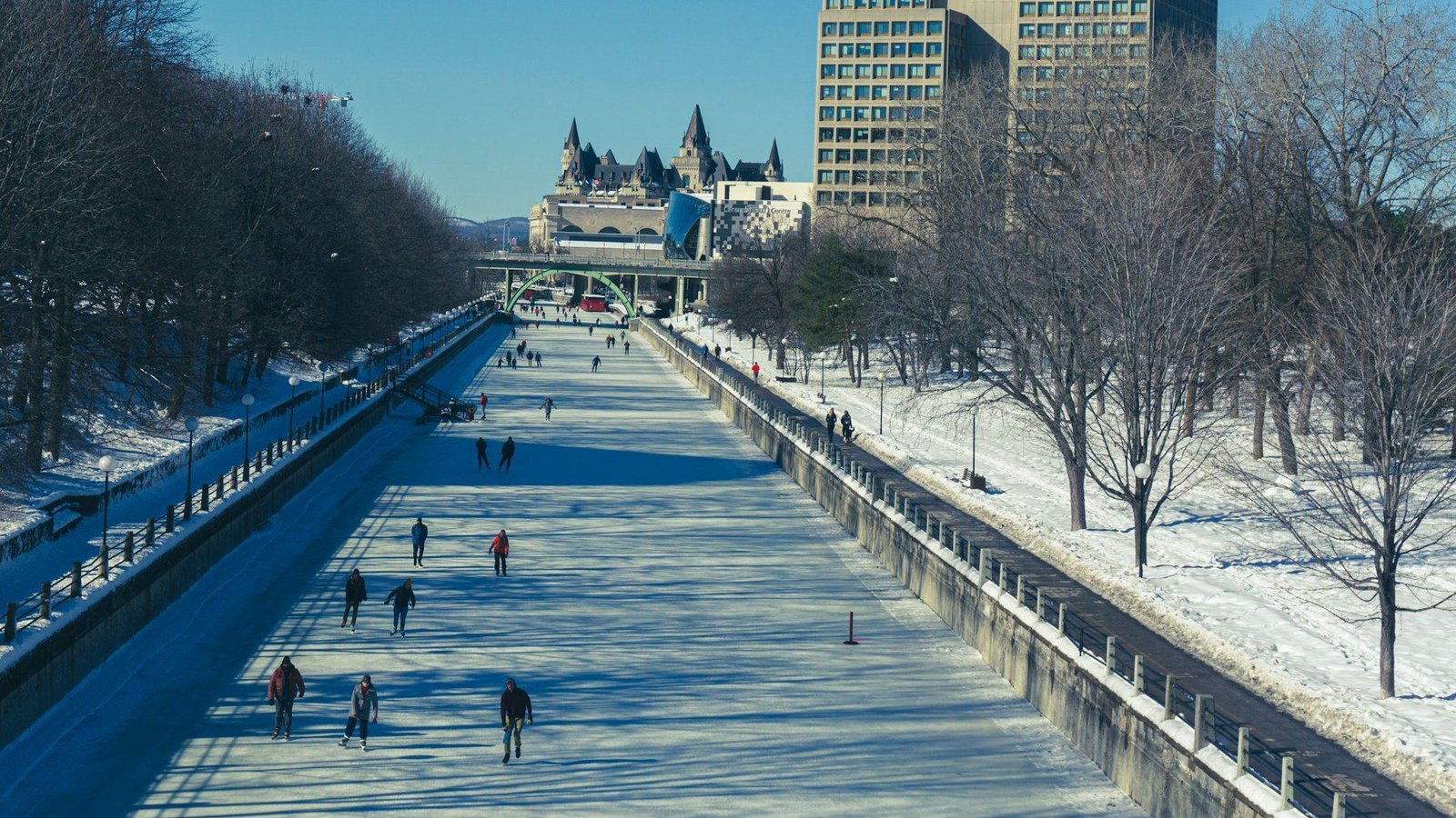 Skaters on the frozen Rideau Canal in Ottawa on a sunny winter day, with the Château Laurier in the distance